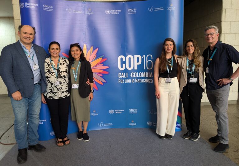 What Is COP16? Learn All About JGI’s Role at This Year’s UN Convention on Biological Diversity A photo of six people of varying appearances standing for a photo around a large blue sign that says, "COP16 / Cali, Colombia / Paz con la Naturaleza."